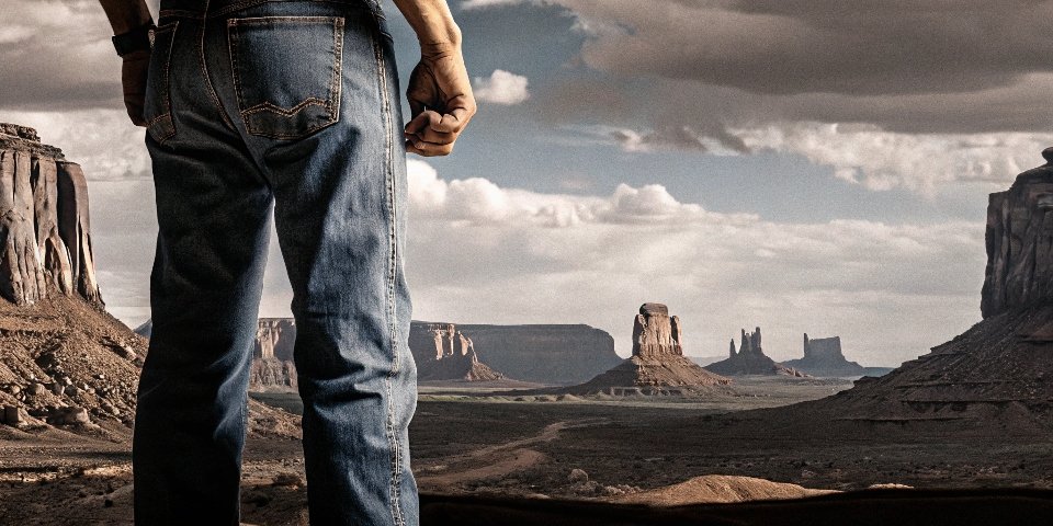 A classic American landscape like Monument Valley with a man in the foreground wearing timeless blue jeans.
