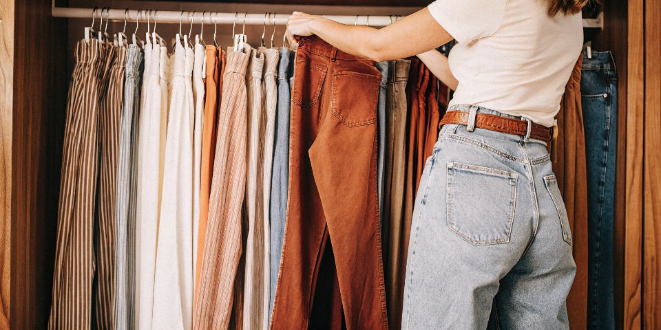 A person stands in front of a closet, thoughtfully choosing a shirt to go with their blue jeans, illustrating smart color pairing.