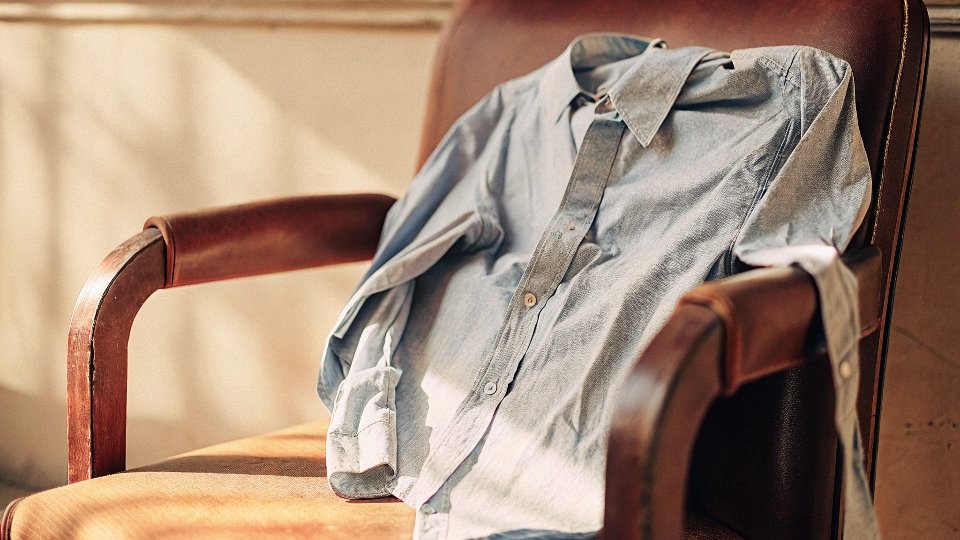 A heavily wrinkled light blue chambray shirt tossed on a chair, highlighting its main disadvantage.