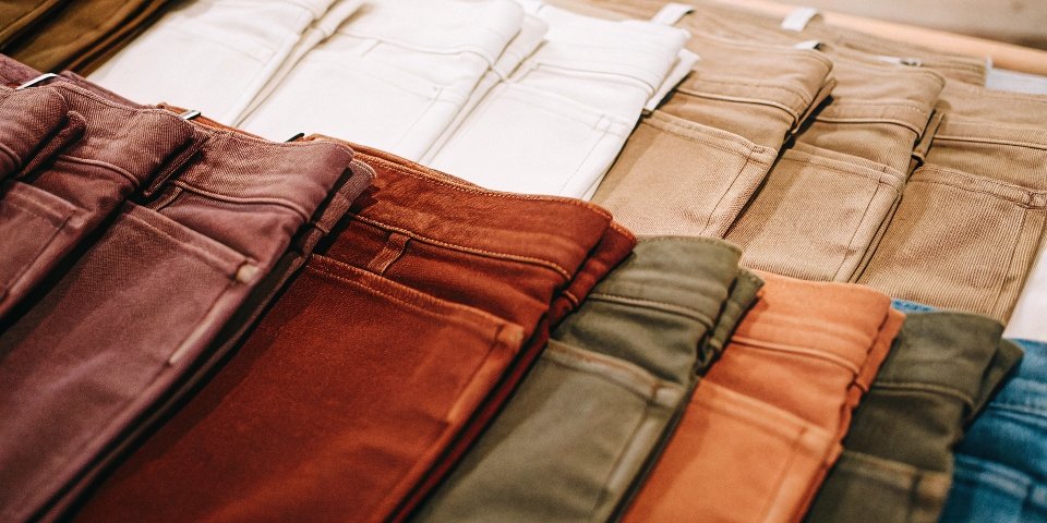A rainbow array of colored denim jeans folded neatly in a stack.
