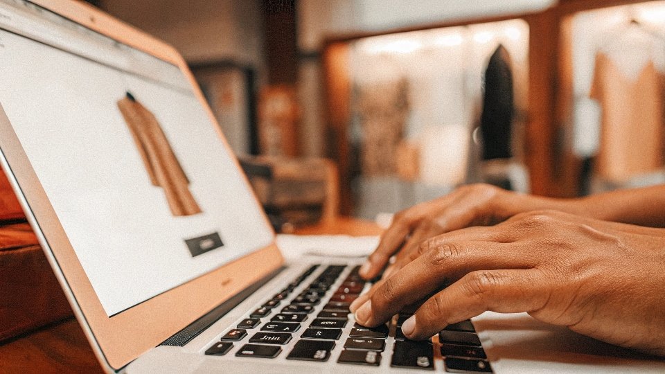 A person's hands typing "quality clothing manufacturer" into a search bar on a laptop.