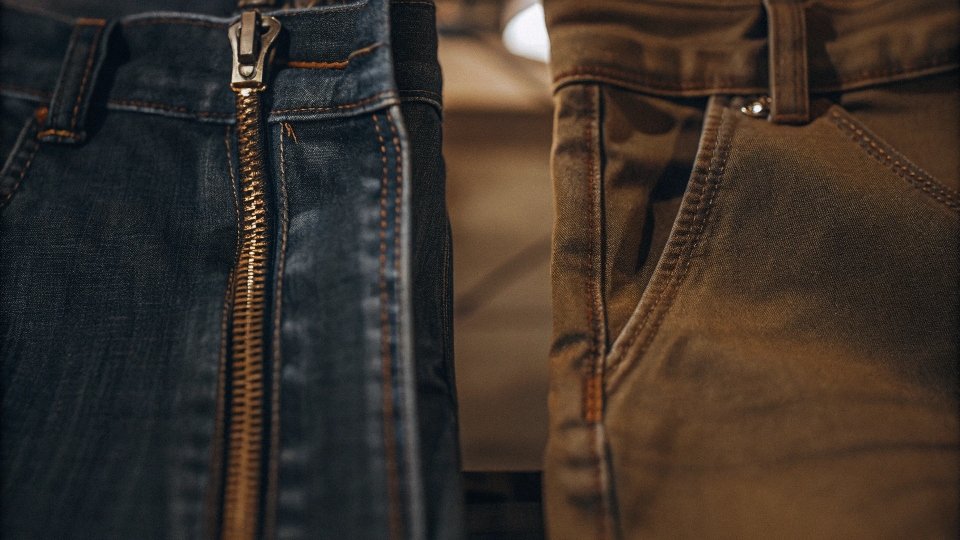 A side-by-side comparison of a high-quality YKK zipper next to a cheap, generic, and broken zipper on a pair of fake jeans.
