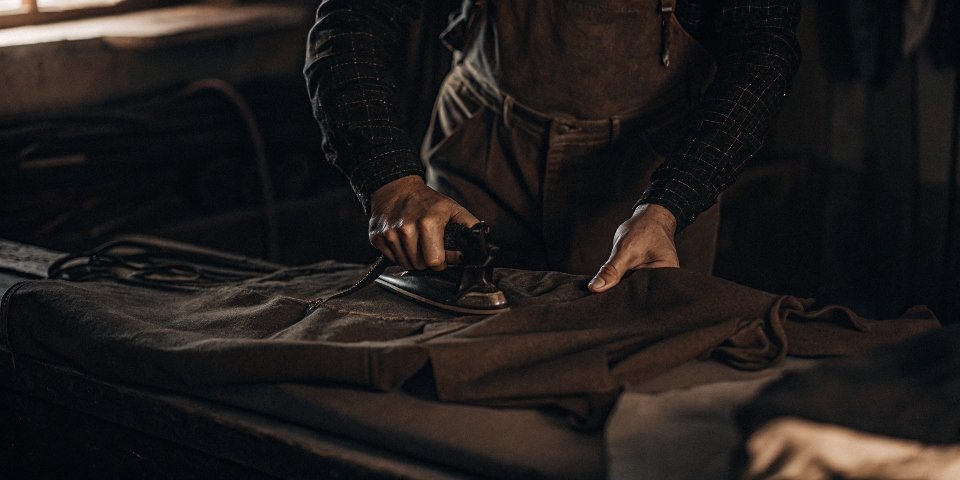 A vintage black-and-white photo of a person from the 1940s or 1950s ironing a pair of crisply starched trousers.