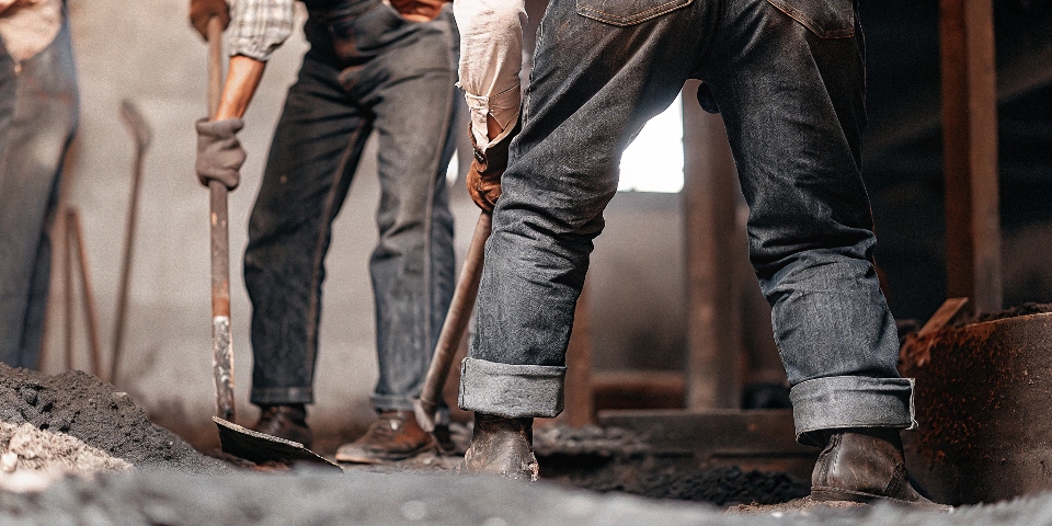 A vintage-style photograph depicting 19th-century workers in dark, sturdy-looking blue jeans.