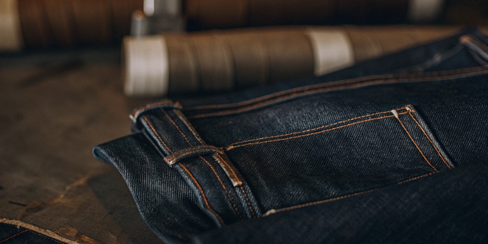 A close-up shot showing the texture of indigo-dyed denim fabric, highlighting the white core of the cotton threads.