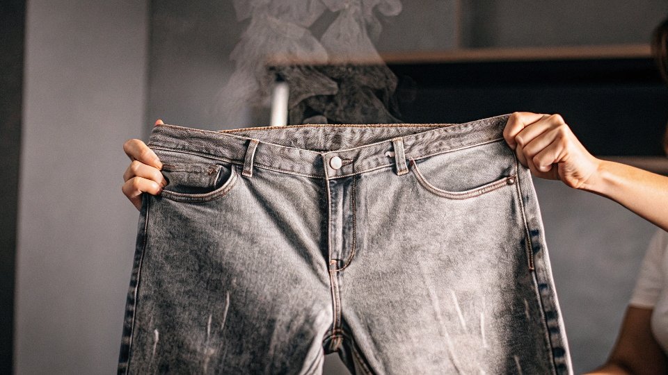 A person holding a pair of jeans and looking at them with a confused expression.