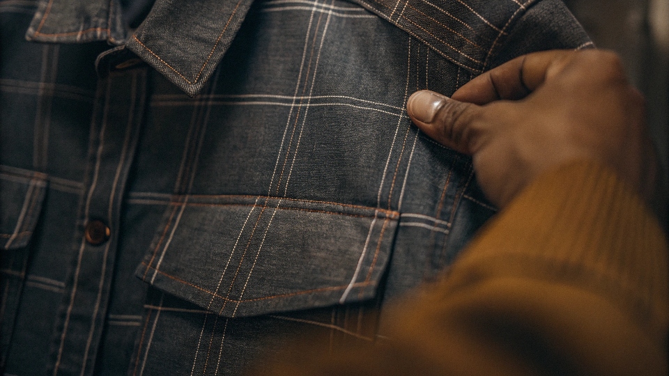 A person's hand feeling the texture of a chambray shirt, illustrating its softness, with a rugged denim shirt in the background for contrast.