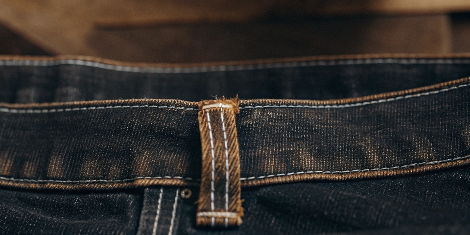 A detailed close-up shot of a stretched-out waistband on a pair of jeans, showing the tiny, broken elastic fibers.