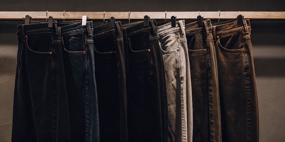 A rack of jeans in multiple colors: classic blue, black, grey, white, and olive green.