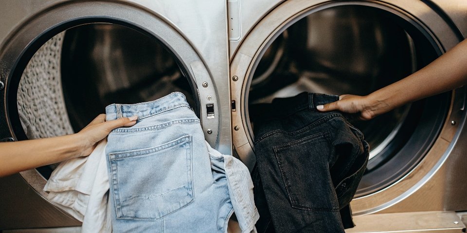 A washing machine with a clear "Warning" sign, showing a blue jean and a black jean being kept separate.
