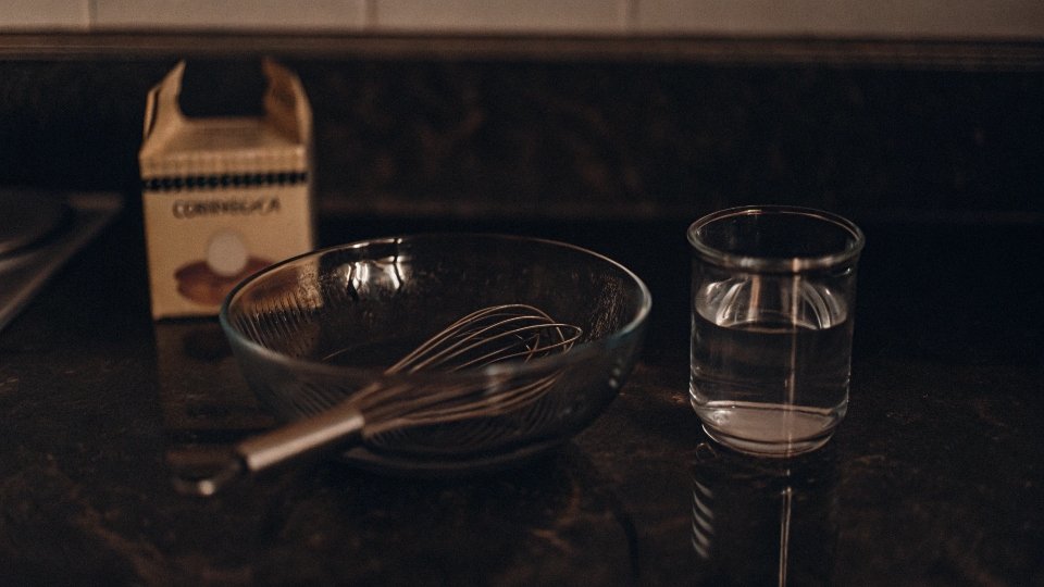 A simple kitchen setup showing a box of cornstarch, a bowl of water, and a whisk, ready for making DIY starch.