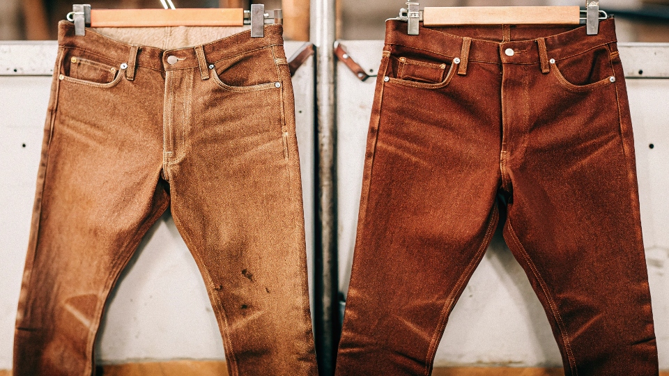 A close-up of a pair of stiff, dark, unwashed raw denim jeans, highlighting the rigid texture.
