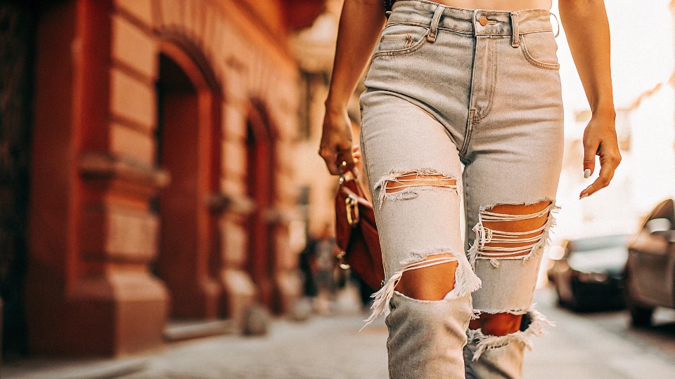 A stylish person wearing fashionable ripped jeans on a city street.