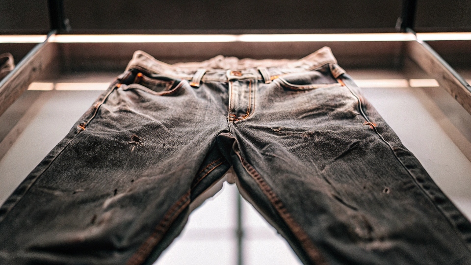A very old, weathered pair of Levi's jeans displayed under spotlight in a glass museum case.