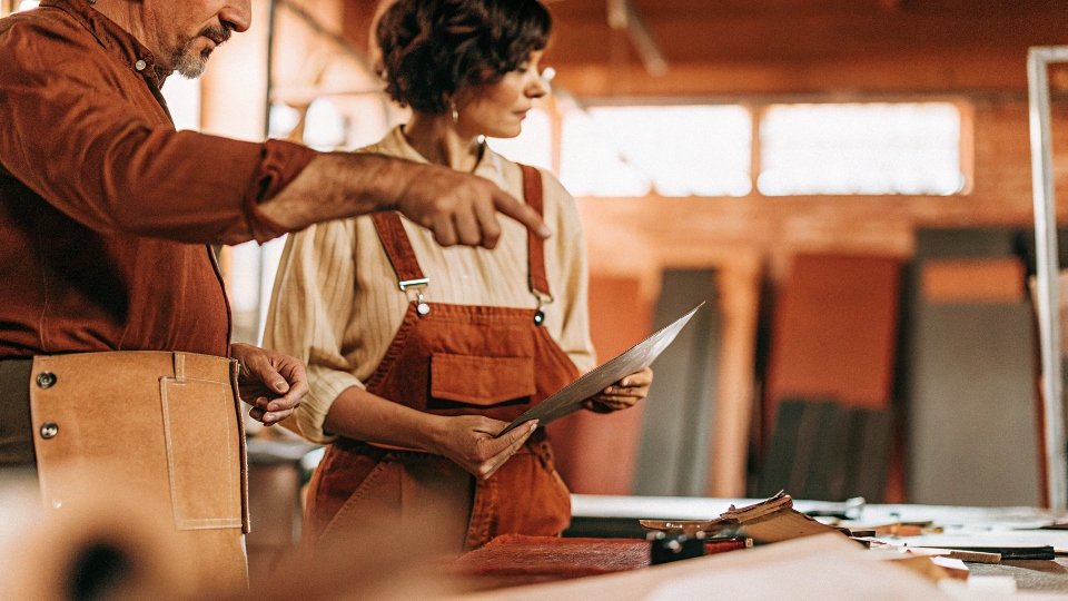 A designer and a factory manager collaborating over denim fabric swatches in a well-lit workshop.