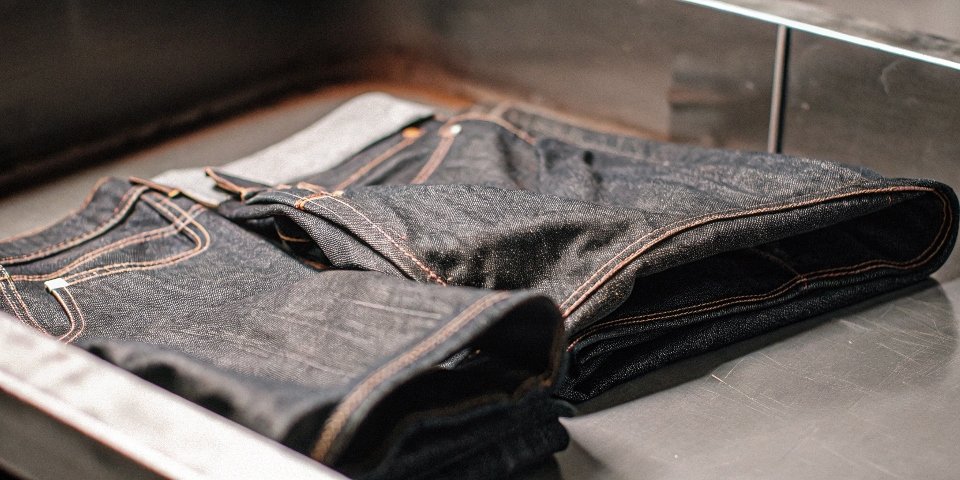 A pair of dark denim jeans being carefully folded and turned inside out before washing.