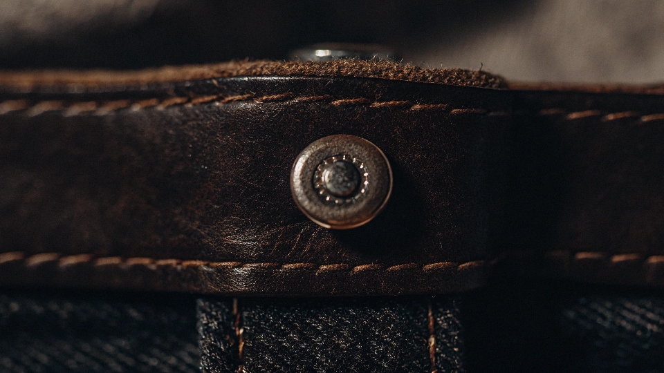 A close-up shot of a custom-designed jean rivet with a brand's logo embossed on the metal cap.