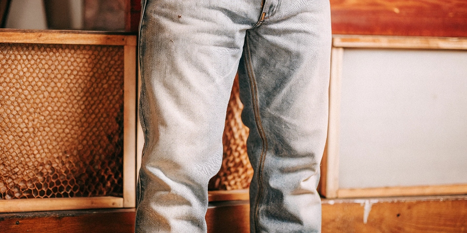 A beautifully faded pair of selvedge jeans showing high-contrast 'whiskers' on the lap and 'honeycombs' behind the knees.