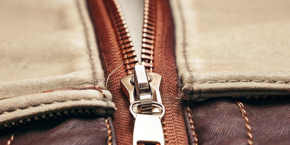 A close-up shot of a high-quality metal zipper on a pair of dark denim jeans.