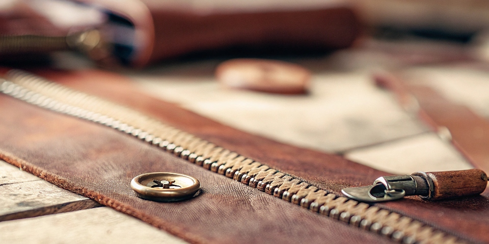 A close-up on a workbench showing a classic metal button and a modern zipper, symbolizing tradition vs. modernity.