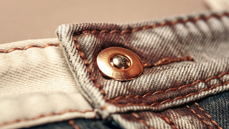 A detailed close-up shot of a copper rivet on the corner of a classic blue jean pocket.