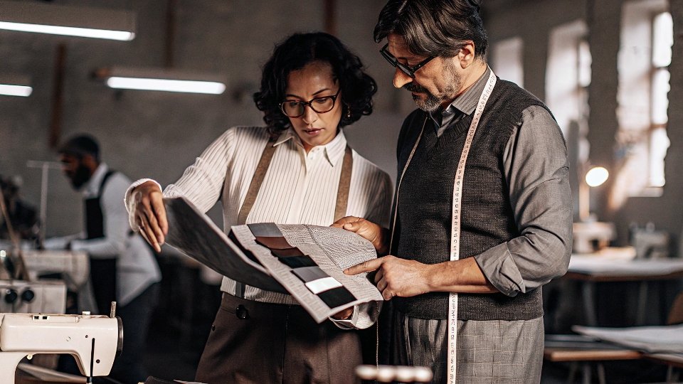 A clothing designer carefully examining fabric swatches with a factory manager.