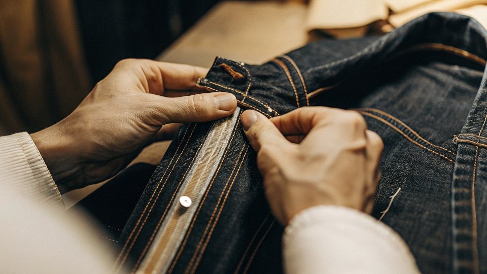 A close-up shot of a person's hands examining the stitching on a high-end denim jacket.