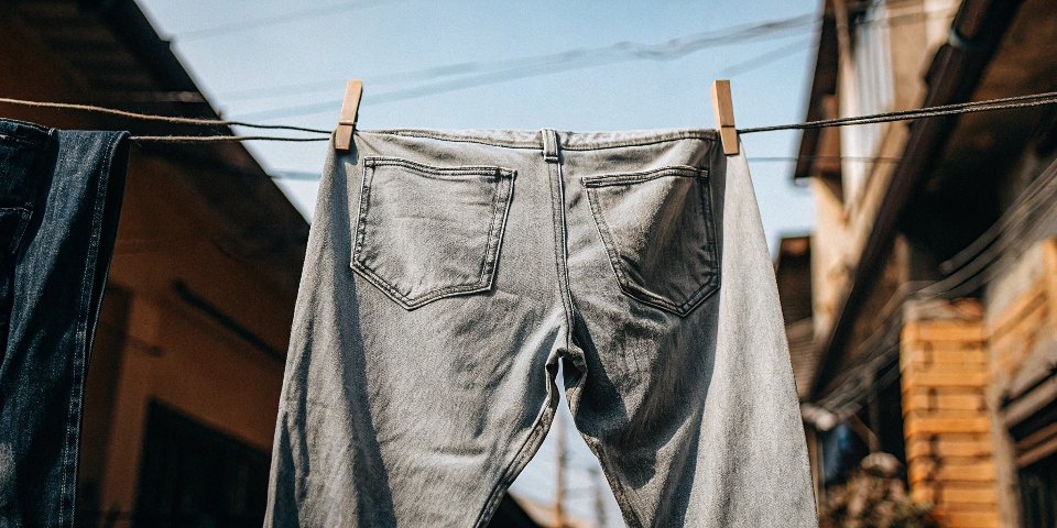 A pair of jeans hanging on a clothesline outdoors with a clear blue sky in the background.