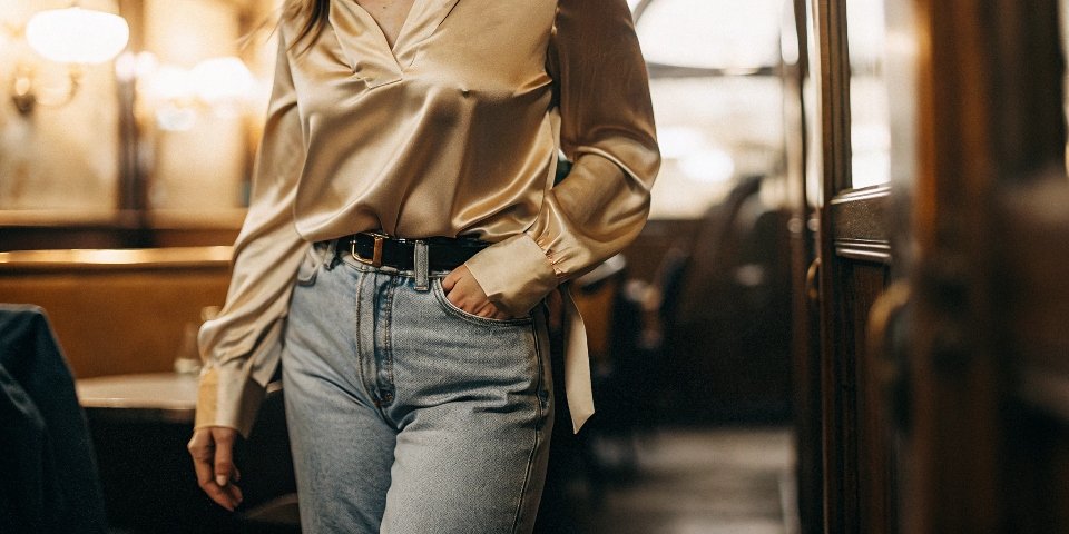 A stylish person wearing a luxurious silk shirt tucked into a pair of casual, well-fitting blue jeans.