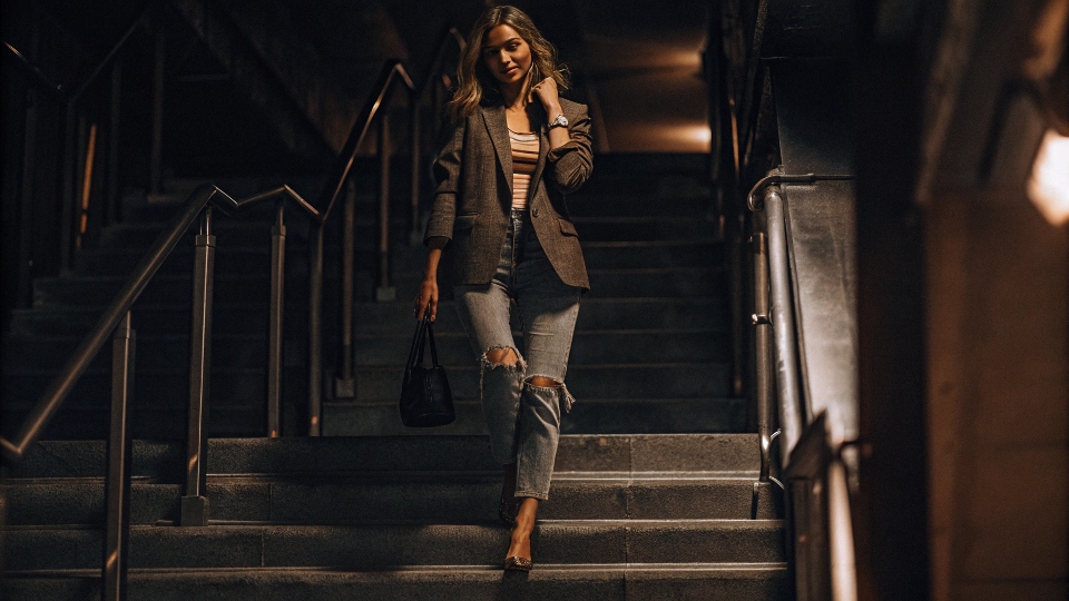 A 50-year-old woman confidently wearing ripped jeans with a tailored jacket and chic accessories.
