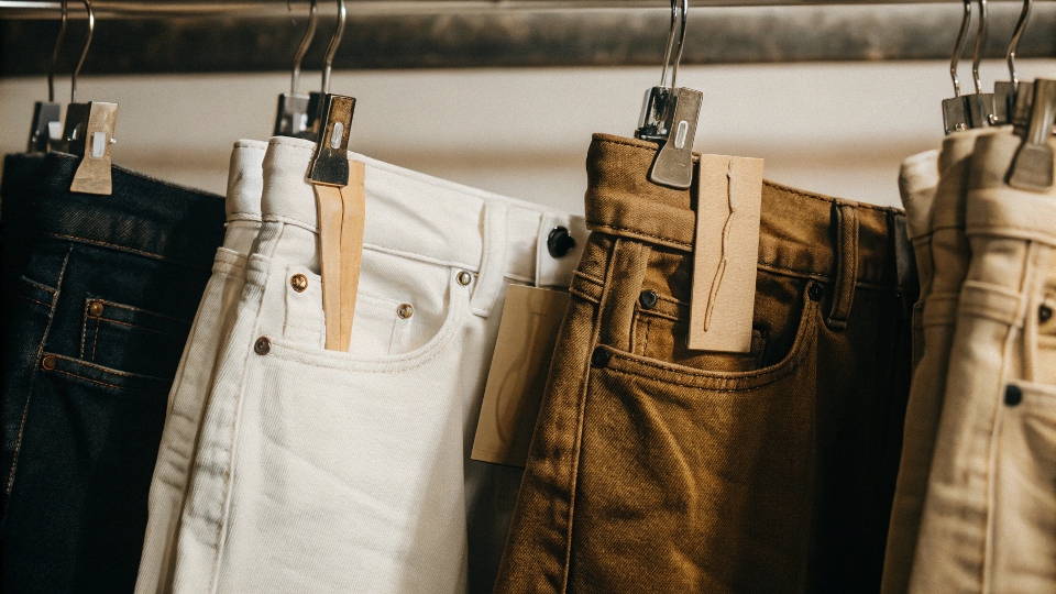 A clothing rack featuring several pairs of jeans with tags showing "100% Cotton."
