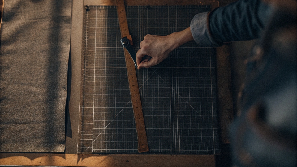 An overhead shot of a cutting mat with a jean leg laid flat, being cut into precise squares with a rotary cutter and acrylic ruler.