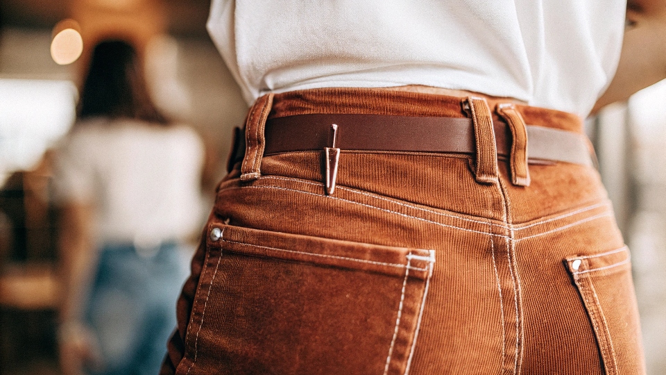 A close-up of the back of a jean waistband showing two small, neat darts sewn in.