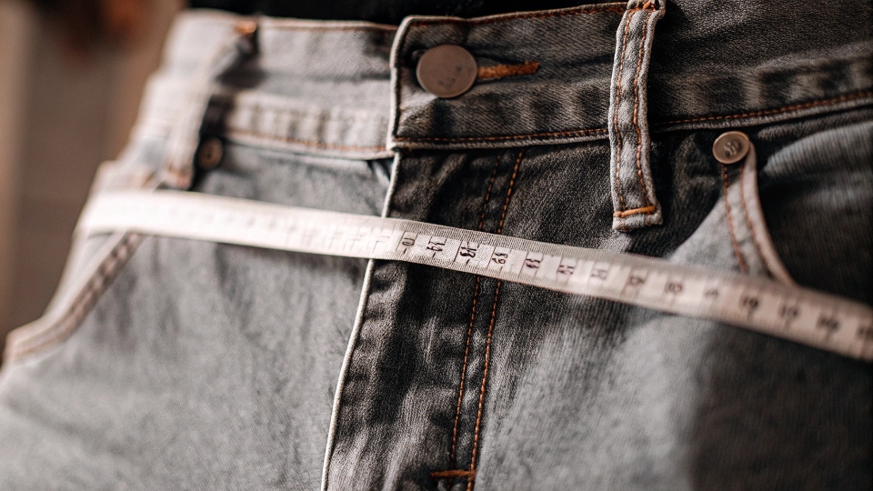 A tape measure laid across the waistband of a size 32 jean, showing the actual measurement is closer to 33 inches.