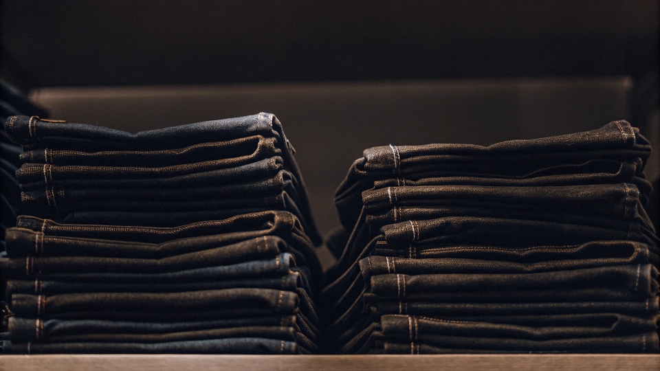 A stack of neatly folded Kirkland Signature blue jeans on a shelf in a Costco store.