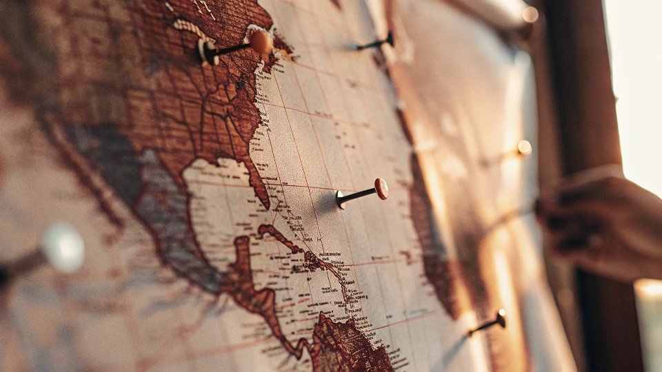A world map with an old-fashioned pin on Kansas, USA, and modern factory icons pinned on Mexico and India.