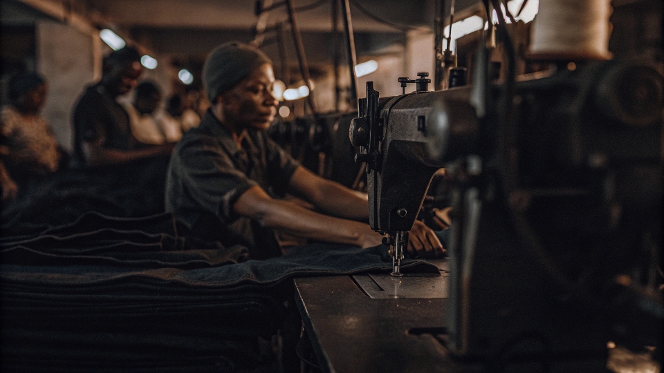 a factory worker operating an industrial sewing machine to assemble jeans