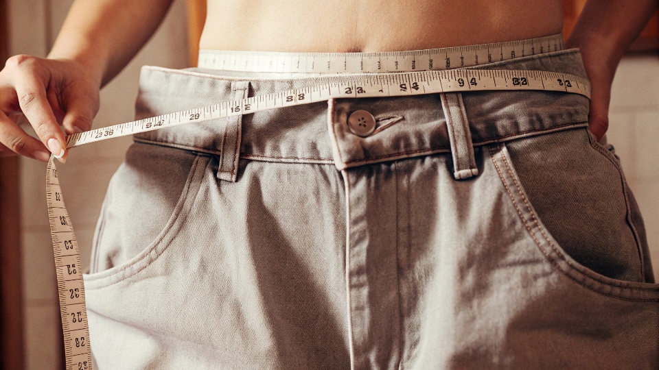 A clothing measuring tape laid across the waist of a pair of baggy jeans.