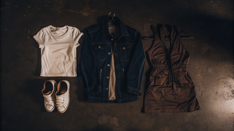 A flat lay arrangement showing a blue denim jacket with a white T-shirt, a simple dress, sneakers, and heels.