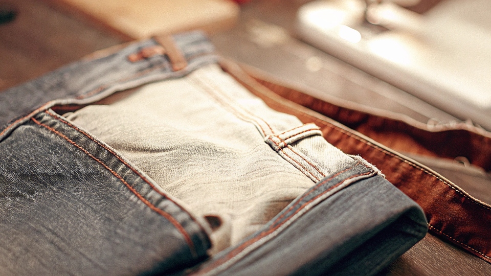 A close-up of a pair of jeans turned inside-out, with a new denim patch being sewn into the crotch area.