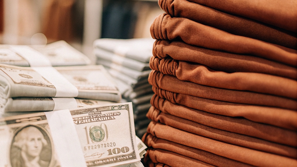 a stack of US dollar bills next to a pile of folded jeans