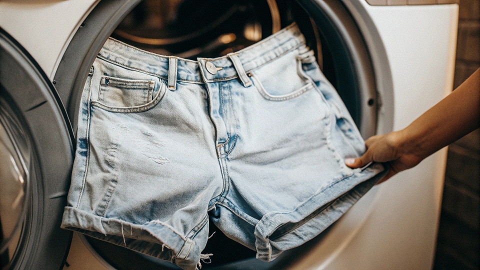 A pair of newly cut jean shorts tumbling inside a washing machine to create a frayed edge.
