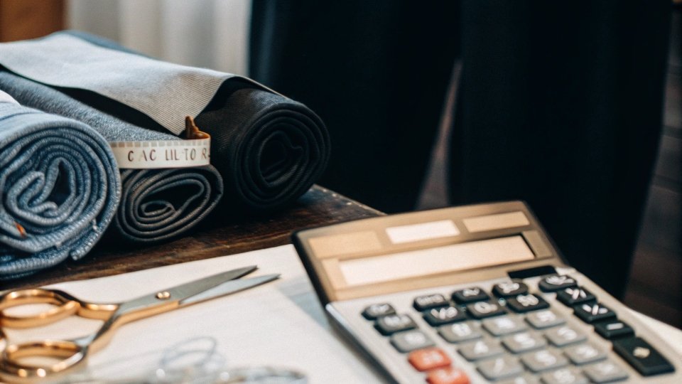 Calculating Jean Manufacturing Costs a calculator and rolls of denim fabric on a cutting table