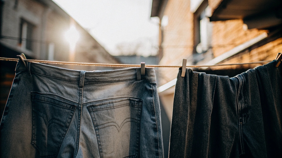 Jeans hanging on a clothesline to air dry, with the sun in the background, symbolizing a gentle care process.