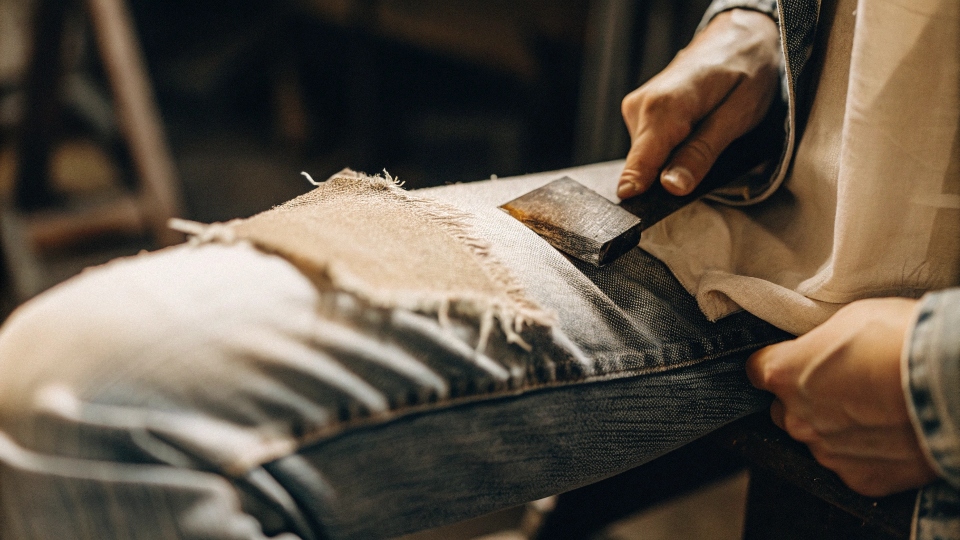 A close-up shot of someone using a block of sandpaper to fade the thigh of a pair of jeans.