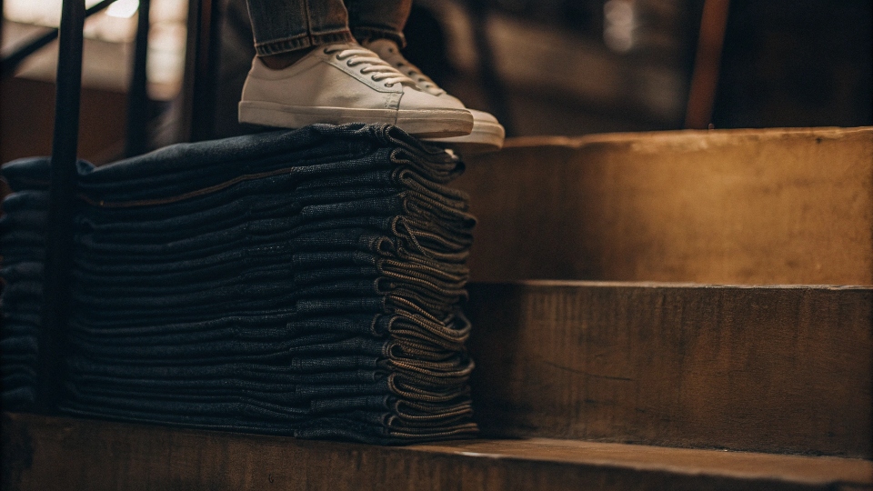 A close-up shot of perfectly stacked jeans sitting on top of a clean sneaker.