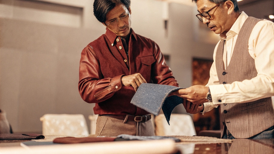 A Western designer and a Chinese factory manager reviewing a denim fabric swatch together.