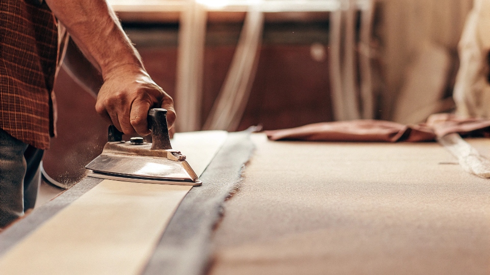 A person using a hot iron to press and activate a strip of fusible bonding web between a jean leg and a fabric panel.