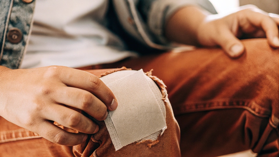 Fine-grit sandpaper being rubbed on the knee of a pair of jeans to create a soft, worn-in texture.