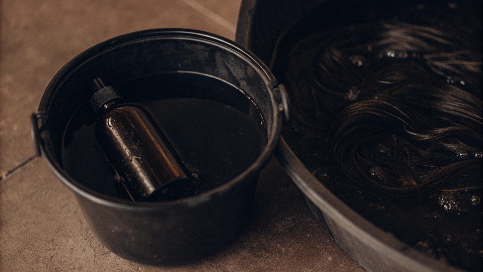 A bottle of hair conditioner next to a bucket filled with water.